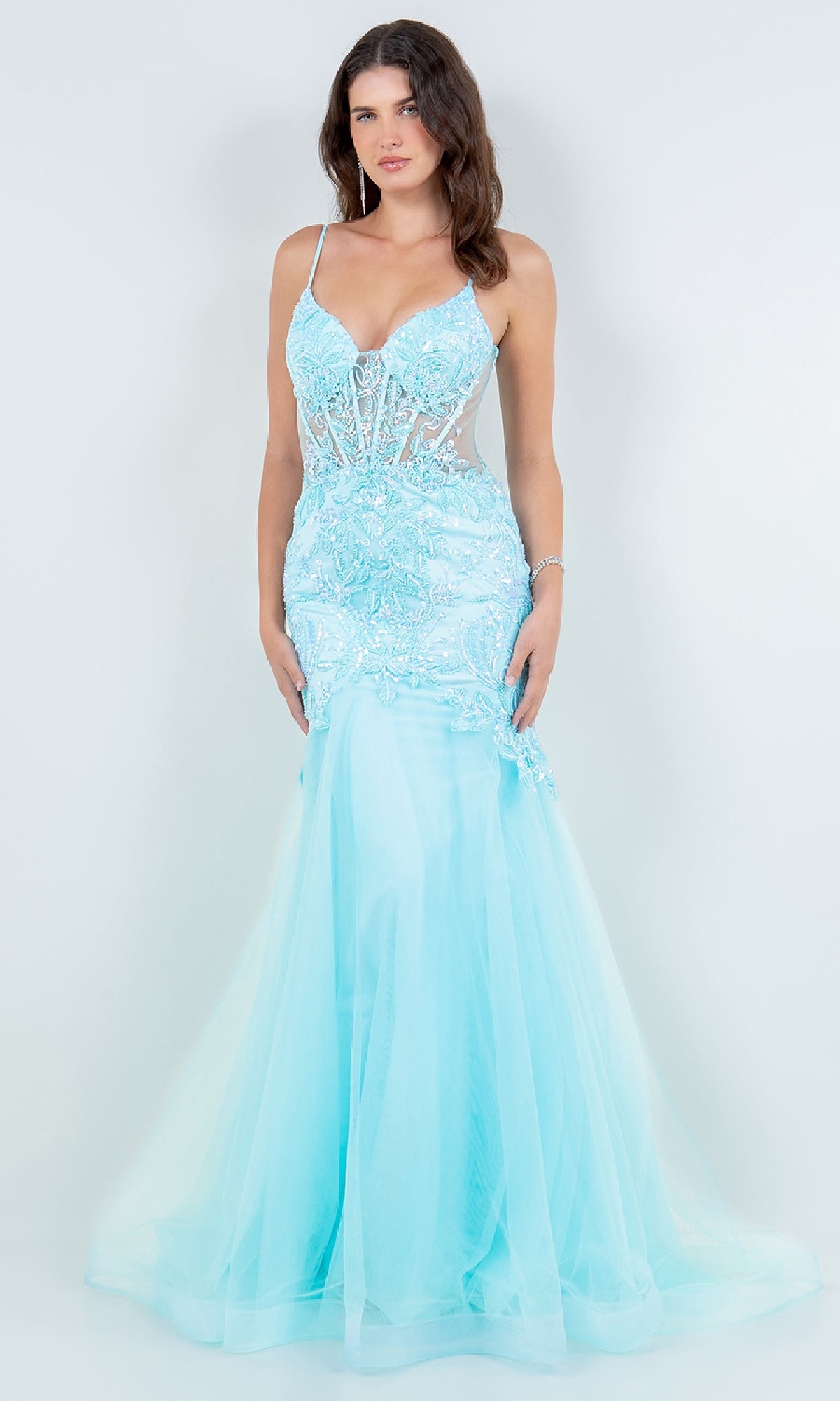 A woman models the Cinderella Couture 8276J, a light blue floor-length sequin mermaid prom dress with sheer bodice and floral embellishments, standing against a plain white background.
